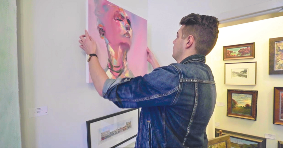 Internship student hanging a painting in a gallery